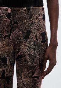 Pantaloni neri con motivo a linee floreali dorate, chiusura con bottone rosa, taglio aderente e tessuto con sottile effetto satinato.