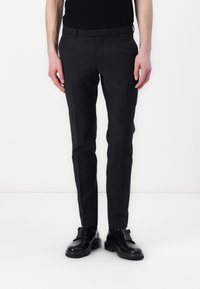 Svarta skräddarsydda byxor med smal passform, slät front, jämn textur och minimala detaljer, tillsammans med svarta skor, stående mot en vit bakgrund.