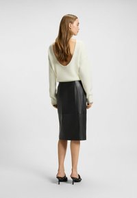 Weißer Pulli mit offenem Rücken und langen Ärmeln, kombiniert mit einem figurbetonten schwarzen Leder-Midirock. Das Outfit zeichnet sich durch eine glatte Textur und einen maßgeschneiderten Look aus.