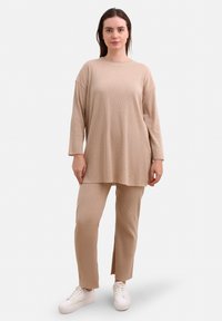 Beige ribbet strik langærmet tunika parret med matchende ribbet bukser, der har en afslappet pasform og sideudskæringer. Båret med hvide sneakers.