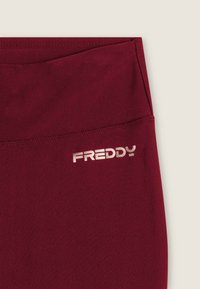 Leggings sportivi color granata realizzati in un tessuto morbido e leggermente lucido. Presentano un logo tonale "FREDDY" in argento metallizzato sulla vita.