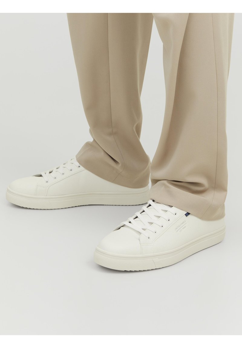 Białe skórzane sneakersy z okrągłym czubkiem, płaską podeszwą i sznurowanym zapięciem. W połączeniu z beżowymi spodniami o dopasowanym kroju, charakteryzującymi się gładką fakturą.