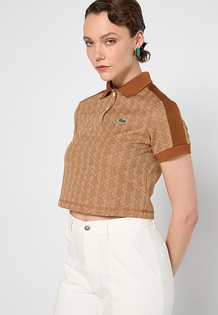 Camiseta polo corta de color marrón con un diseño de diamante texturizado, cuello y mangas marrones en contraste, que presenta un pequeño logo verde.