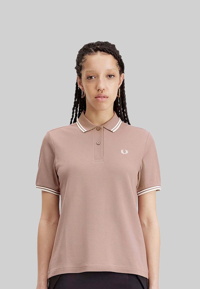 Polo a maniche corte in rosa polveroso con strisce bianche a contrasto sul colletto e sui polsini, con un piccolo logo sul petto.