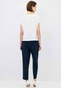 Top blanco de manga corta con patrón texturizado, combinado con pantalones azul marino, mostrando un ajuste relajado. Zapatos de tacón alto completan el look.