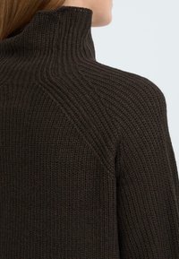 Brauner, gestrickter Rollkragenpullover mit strukturiertem Rippenmuster, der einen hohen Kragen und eine taillierte Silhouette aufweist, betont Wärme und Komfort.