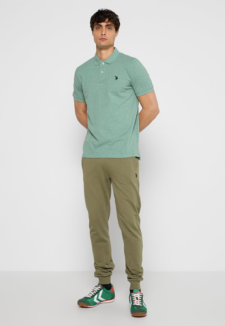 Grünes Poloshirt und olivfarbene Jogginghosen. Das Poloshirt hat einen klassischen Kragen und ein dezentes Logo; die Jogginghosen verfügen über elastische Bündchen und einen Kordelzugbund.