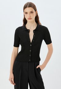 Cardigan corto de manga corta negro con cuello y una fila de botones negros, que presenta un ajuste slim y una tela texturizada.