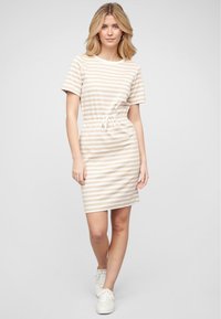Randig t-shirtklänning i beige och vitt, med dragsko i midjan, korta ärmar och knälång längd. Bärs med vita sneakers.