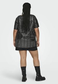T-shirt oversize nera con paillettes e maniche corte, caratterizzata da una vestibilità ampia e una gonna mini nera a strati, abbinata a stivali neri alti fino al ginocchio.