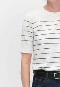 Hvid kortærmet top med vandrette navy striber, rund halsudskæring, glat tekstur, parret med et sort bælte og mørke denimbukser.