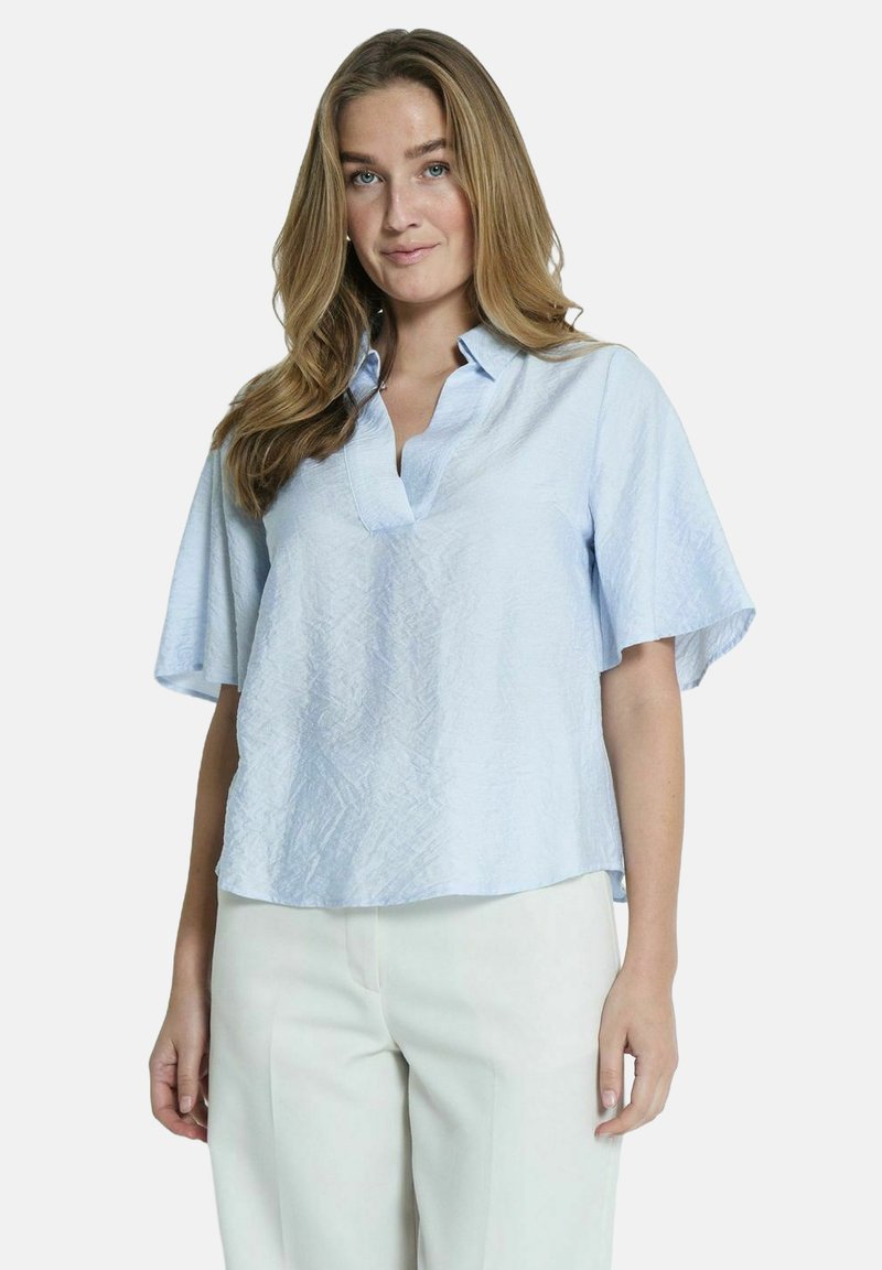 Blouse texturée bleu clair avec un col et des manches courtes et larges. Associée à un pantalon de couleur crème, au fit ample et décontracté.