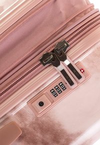 Rosa Koffer mit doppelten Metallreißverschluss-Zippern, einem Zahlenschloss mit nummerierten Scheiben und einem strukturierten synthetischen Außenmaterial.