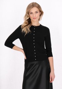 Cardigan nero con maniche a tre quarti, caratterizzato da una fila di bottoni in perla sintetica bianchi sulla parte frontale. Tessuto in maglia morbida, design senza colletto.