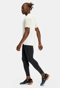Lys grå træningsbluse, sorte tætsiddende leggings og blå løbesko med orange detaljer. Outfitten fremhæver et strømlinet design.
