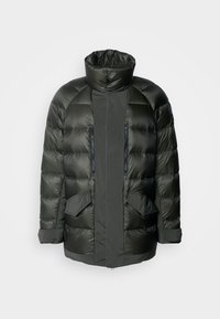 Chaqueta acolchada de color verde oscuro con un cuello alto, bolsillos con cremallera y una textura acolchada. En la parte frontal tiene dos grandes bolsillos laterales y bolsillos en el pecho con cremallera.