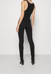 Černé úzké džíny s vysokým pasem a hladkou denimovou texturou, spárované s černým topem bez rukávů. Boty mají blokový podpatek.