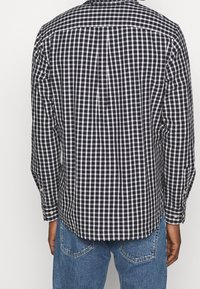 Camicia a quadri in bianco e nero, con maniche lunghe e orlo curvo, realizzata in tessuto leggero con una sottile texture.