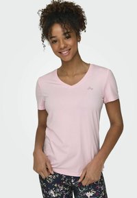Camiseta rosa de manga corta y escote en V, hecha de tejido suave, con un pequeño logo en el pecho, combinada con leggings florales estampados.