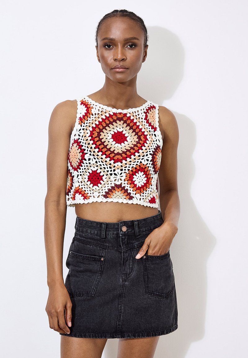Top court en crochet crème avec des motifs géométriques rouges, oranges et bruns ; associé à une jupe en denim noire avec des poches avant.