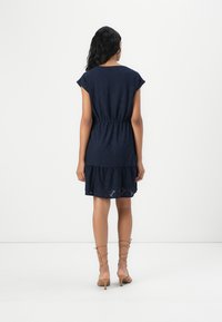 Marinblå klänning med korta ärmar, resårmidja och lager-skirt, med hålmönster och subtil textur. Inga synliga knäppningar.
