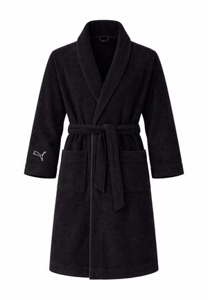 Frau trägt einen schwarzen Fleece-Bademantel mit Schalkragen, Gürtel, Vordertaschen und Puma-Logo am linken Ärmel, lächelt in die Kamera.