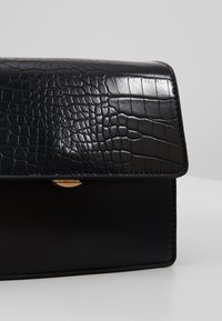 Borsa a spalla nera in ecopelle con texture a coccodrillo, caratterizzata da una forma rettangolare strutturata e un discreto gancio dorato.