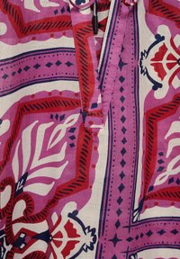 Colorful patterned fabric featuring bold reds, pinks, and navy blue. Design includes floral and geometric shapes with a textured finish.