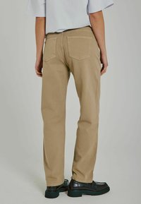 Chinos beige con diseño de corte recto, bolsillos traseros estándares y una textura de tela suave, combinados con zapatos negros y una blusa clara.