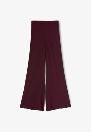 Bordowe spodnie o szerokich nogawkach z fakturowanym wzorem w zygzak i falowanymi obszyciami, ułożone płasko na białym tle.