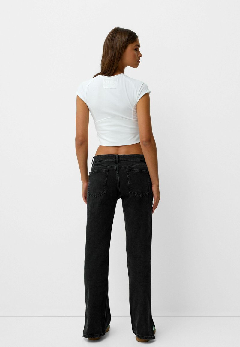 T-shirt bianco cropped con maniche corte, abbinato a jeans neri a campana con un classico design a cinque tasche e dettagli cuciti.