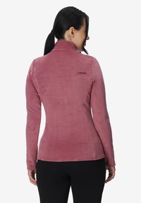 Langærmet pink fleecejakke med høj krave, tætsiddende silhuet og diskret logo på ryggen. Glat tekstur og blødt finish.