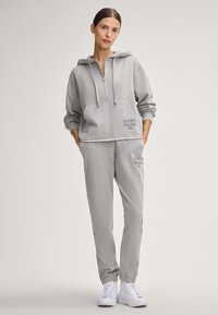 Szary, bawełniany hoodie z kieszenią z przodu i półsuwnym zamkiem. Połączony z dopasowanymi joggerami z elastycznymi mankietami i akcentami w postaci logo. Białe sneakersy.