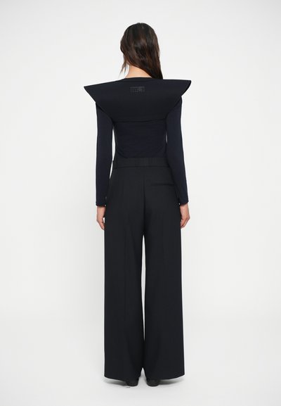 Top preto de manga longa com ombros estruturados e angulares, e um logótipo discreto nas costas, combinado com calças largas com risca de giz de cintura alta.