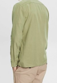 Camicia verde chiaro a maniche lunghe con bottoni. Presenta un colletto classico, orlo dritto e tessuto morbido. Dettaglio dei bottoni visibile sui polsini.
