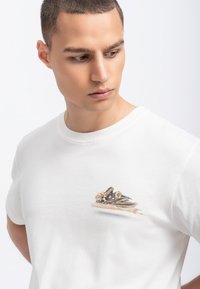 Witte katoenen t-shirt met een kleine, kleurrijke afbeelding van een auto op de borst. De stof is soepel en heeft een klassieke ronde hals.