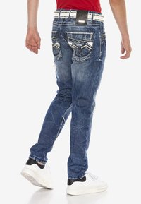 Jeans aus Denim in ausgeblichenem Blau mit schlanker Passform, verziert mit dekorativen Nähten an den hinteren Taschen, abgenutzten Akzenten und einem genoppten weißen Gürtel.