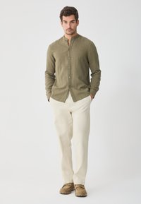 Olive green button-up shirt with a mandarin collar, paired with cream-colored trousers and beige shoes. Smooth fabric with a relaxed fit.