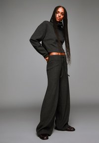 Donkergrijze, cropped hoodie met lange mouwen en een hoge kraag, gecombineerd met wijde, te strikken broek in dezelfde gestructureerde stof.