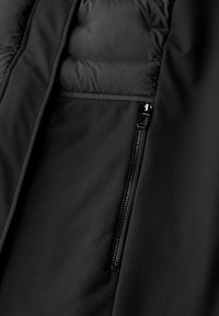 Black puffer jacket interior featuring smooth fabric, quilted sections, and a visible zipper pocket for secure storage.