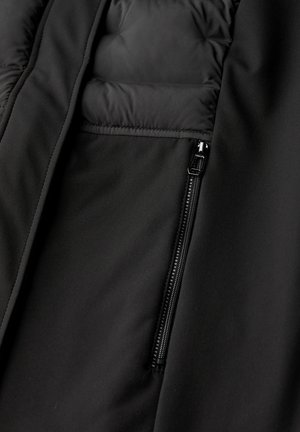 Interior de una chaqueta de plumas negra con tejido suave, secciones acolchadas y un bolsillo con cremallera visible para un almacenamiento seguro.