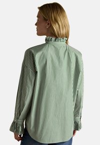 Cămașă cu dungi verzi și albe, cu un guler înalt ondulat și manșete evazate, având o croială lejeră și o textură netedă din bumbac.