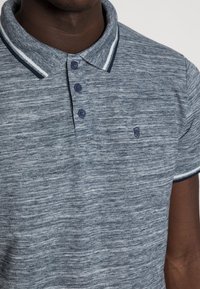 Polo gris texturé avec un plastron à trois boutons, col marine avec des rayures blanches et un petit logo sur la poitrine gauche.