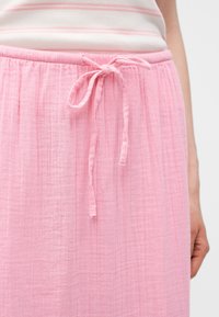 Κοντινό πλάνο ενός ατόμου που φοράει ροζ υφασμάτινη φούστα με δέσιμο στη μέση και ένα ανοιχτό ροζ ριγέ τοπ.