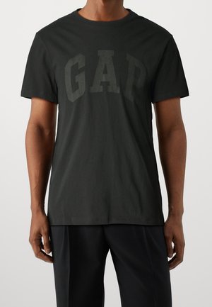 Musta puuvillainen t-paita, jossa suuri haalistunut "GAP"-logo edessä, pyöreä pääntie ja lyhyet hihat, rento istuvuus.