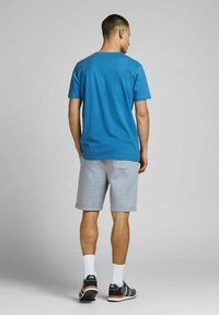 T-shirt blu a maniche corte, pantaloni grigi, scarpe da ginnastica con dettagli arancioni, calze bianche. Design semplice, vestibilità rilassata, materiale misto cotone.