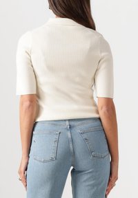 Ribbed cream polo paita lyhyillä hihoilla, vartalonmyötäinen muotoilu, yhdistetty vaaleansinisiin korkeavyötäröisiin farkkuihin, joissa on takataskut ja rento istuvuus.