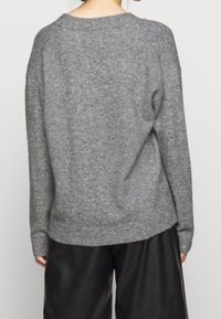 Maglione grigio lavorato a maglia con una consistenza morbida, vestibilità comoda e polsini a costine. Collo e orlo arrotondati, abbinato a pantaloni in pelle nera.