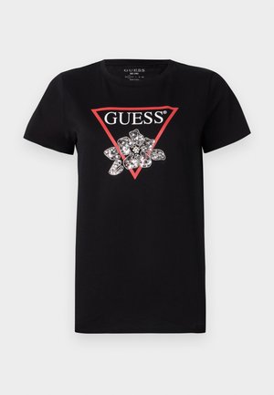 T-shirt noir en coton avec un logo en triangle rouge portant le mot "GUESS" et un design de fleur rehaussé d'accents argentés.