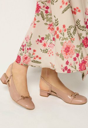 Mujer con zapatos slingback beige de tacón bajo combinados con una falda crema con estampados de flores en rosa y verde.